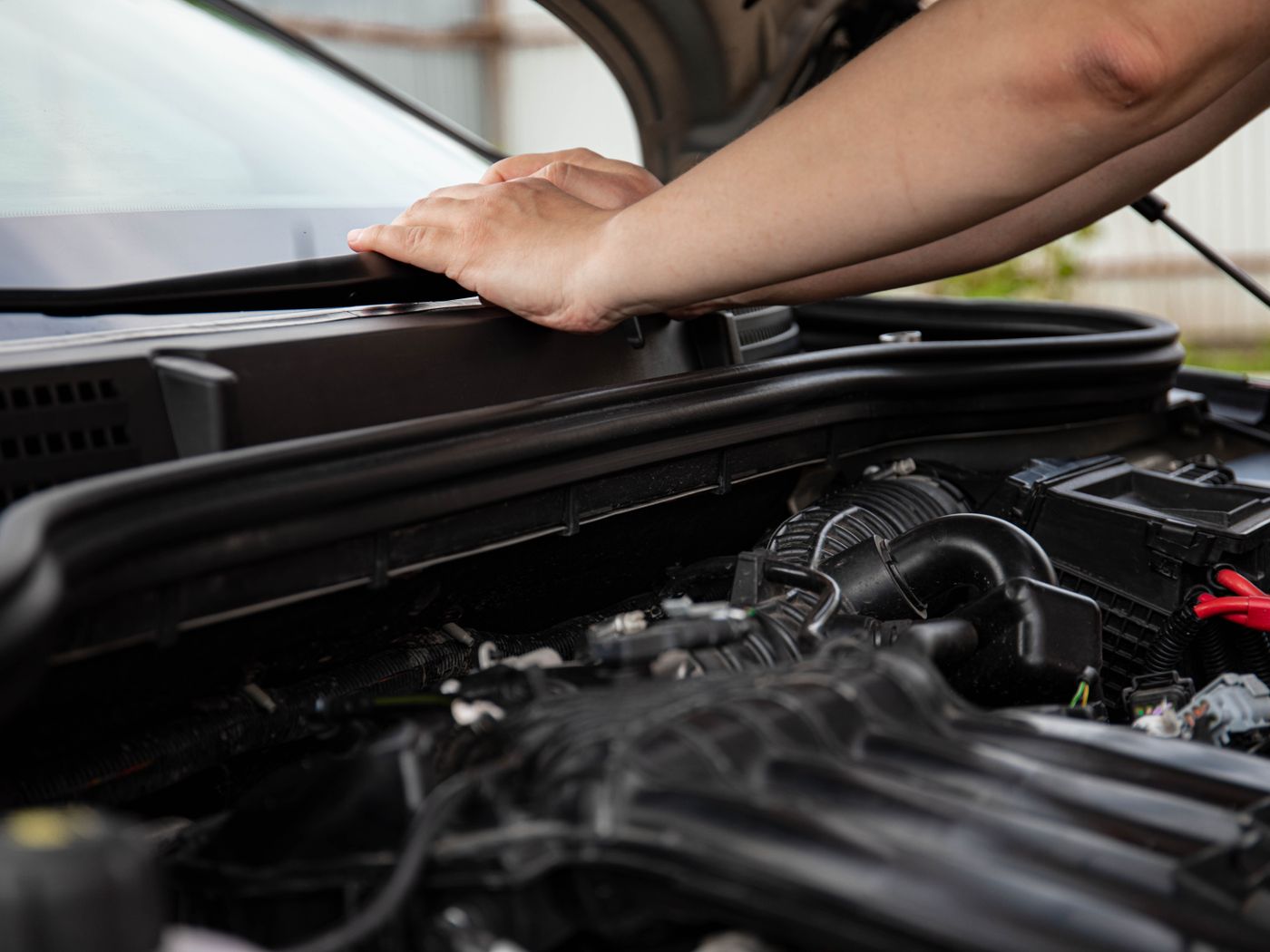 Hand on the open hood of a car with the engine bay exposed for service
